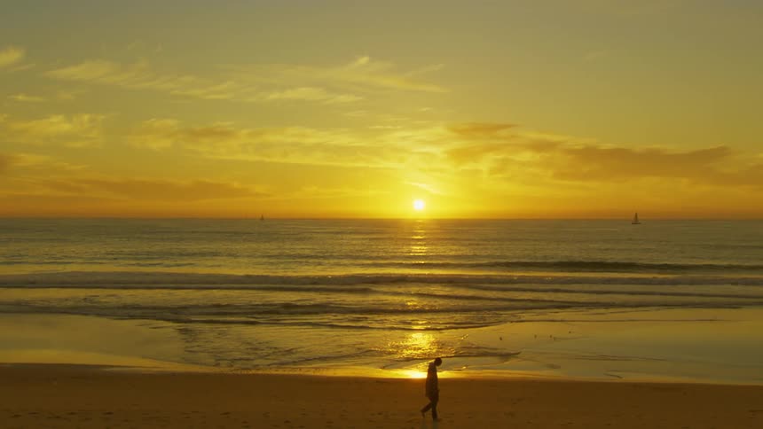 A person walks on the beach at sunset