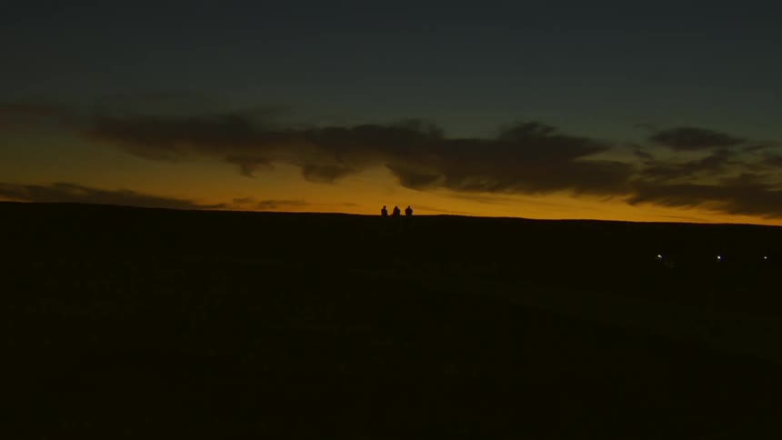 Friends sitting on hill are silhouetted against red sky at night