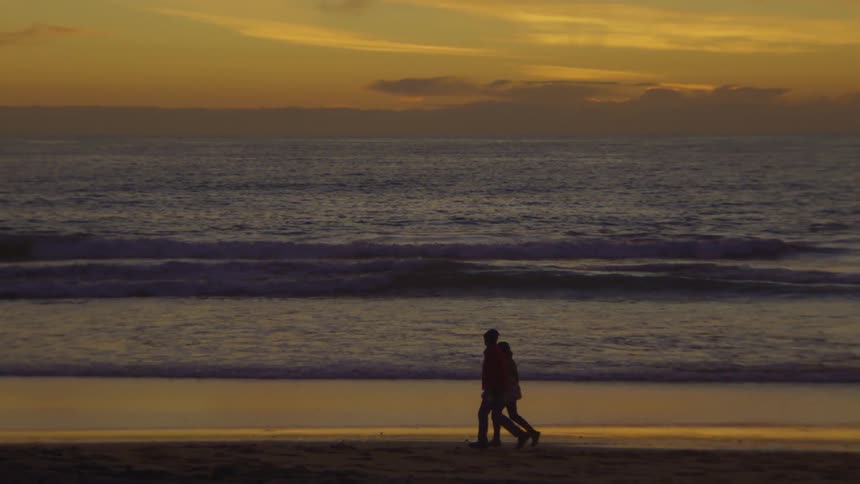 A man and a woman walking on the beach during sunset
