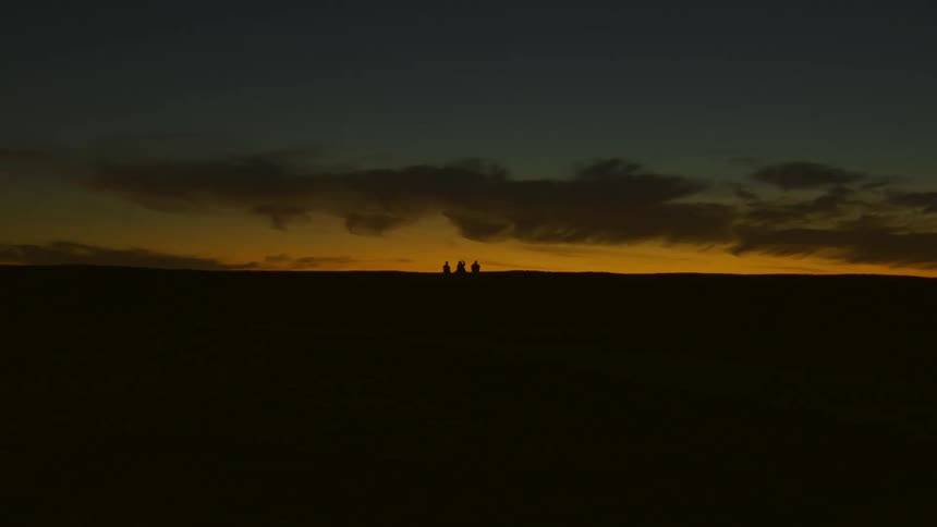 Three people walk across land at dusk or dawn