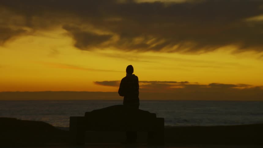 A person filming the landscape with a cell phone during sunset