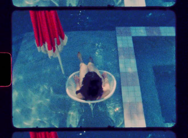 Woman sits in circular chair in the swimming pool near red umbrella