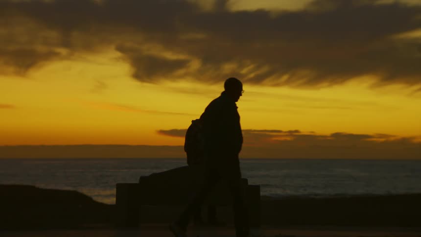 A clip of a man walking past the beach while another is standing by the beach
