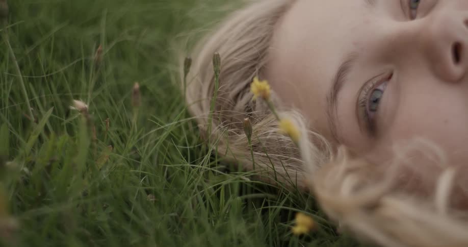 A woman lays in a grassy field with flowers next to her head