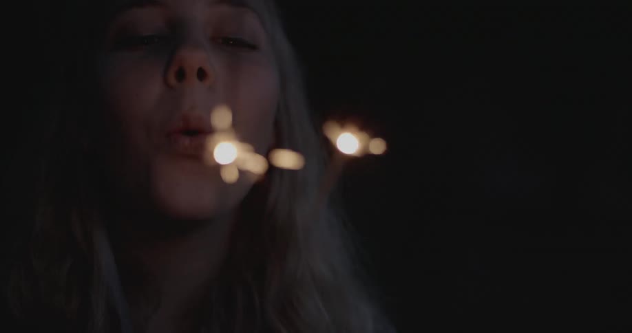 Woman with blond hair blows on sparklers