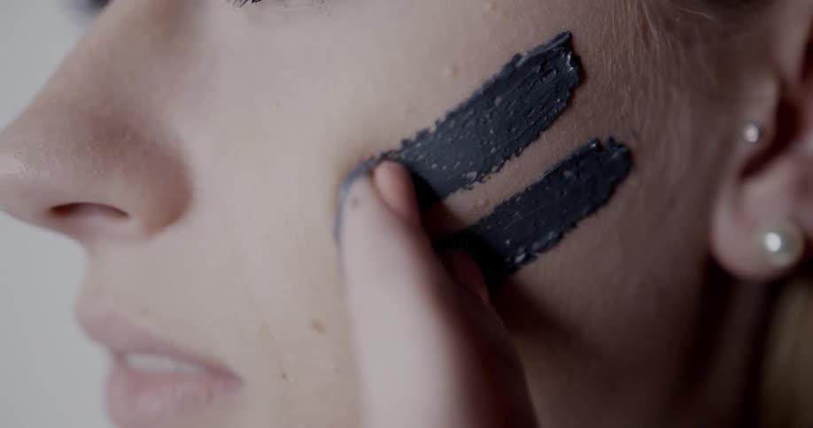 A woman uses her fingers to draw two lines on her face with paint