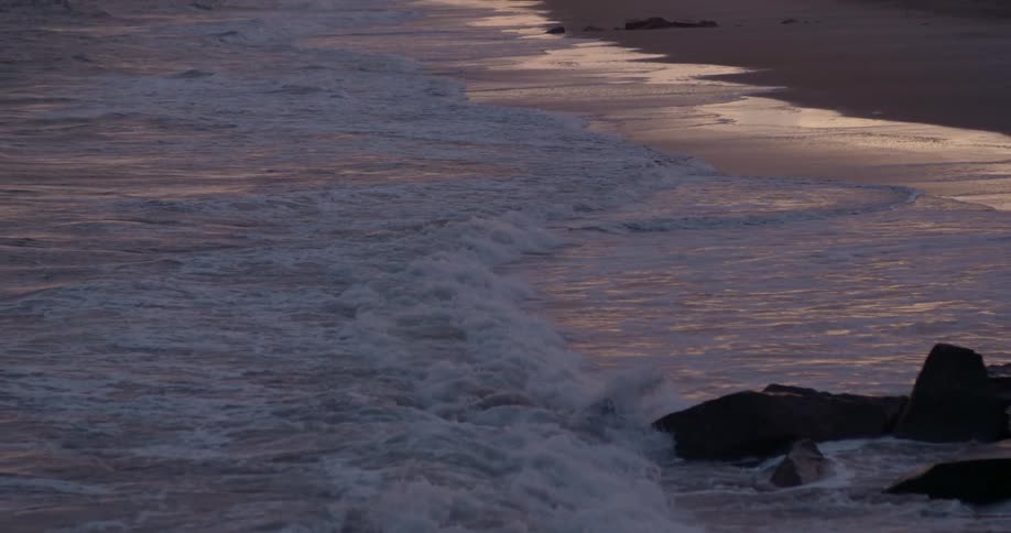 A waves crashes on shore at a beach at sunset