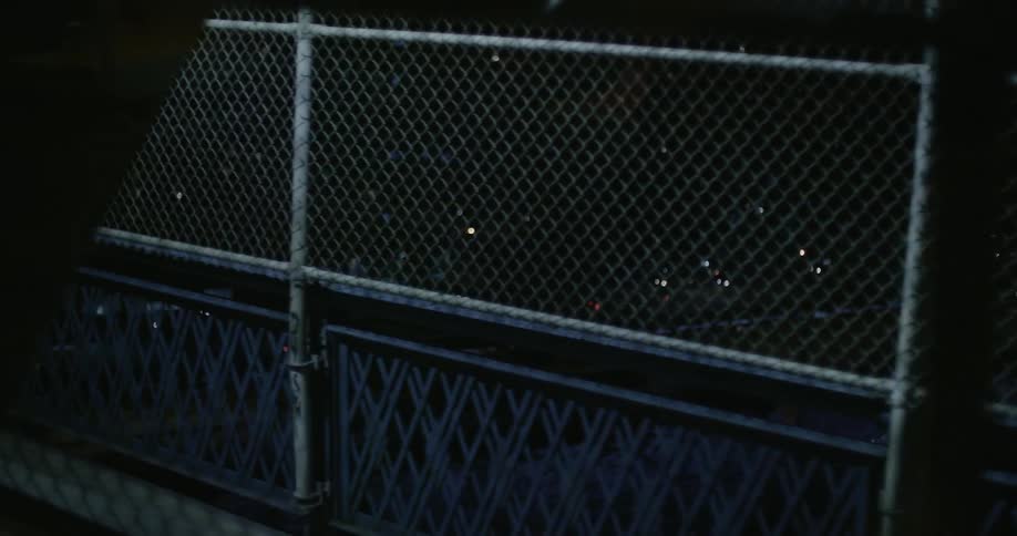 A vehicle is moving over a bridge and seeing the city below through a fence