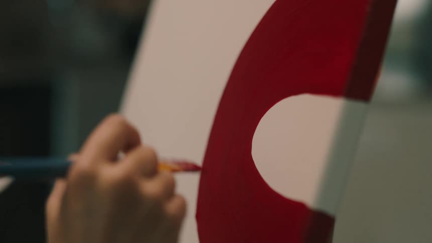 A woman painting a red shape similar to the letter c on canvas with a brush