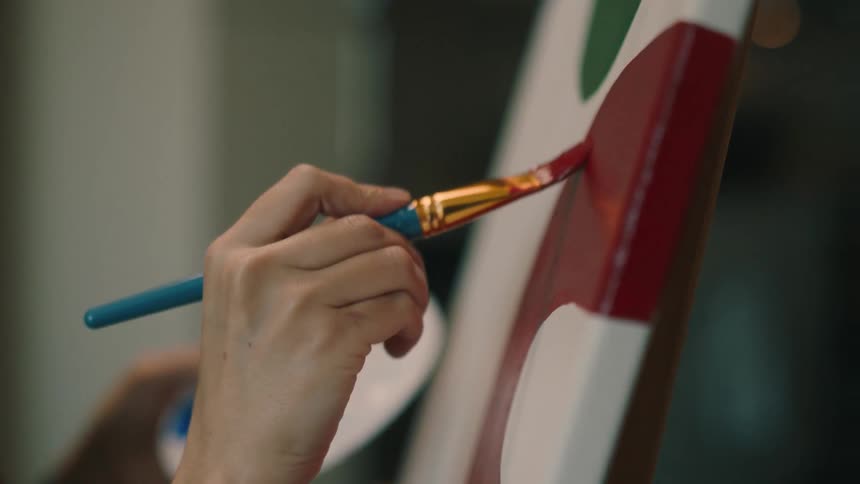 Closeup of a womans hand painting a picture with a brush