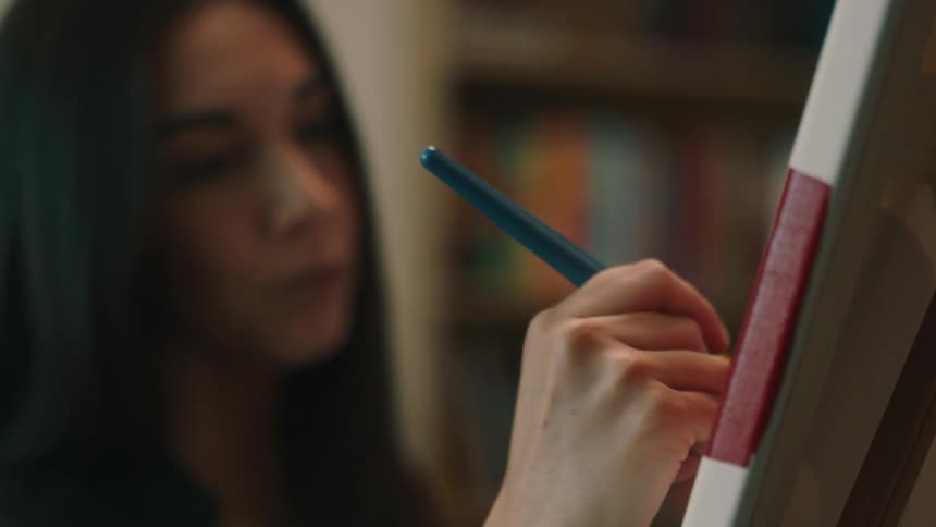 Closeup of a womans hand painting a canvas with a brush