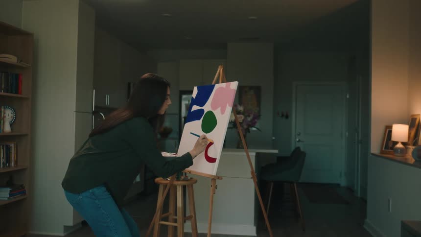 A hispanic woman paints on a canvas in an apartment