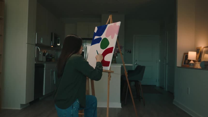 A woman in a room painting colored shapes on canvas with a brush
