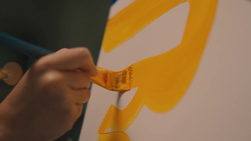 Closeup of a womans hand using yellow paint painting a picture
