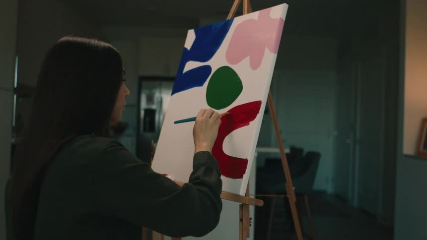A woman paints on a canvas in an apartment