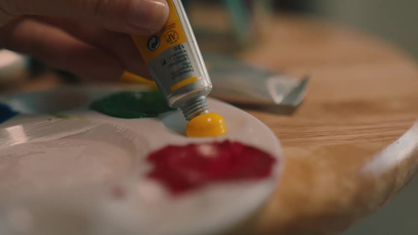 A hand squeezing paint out of a tube onto a palette tray