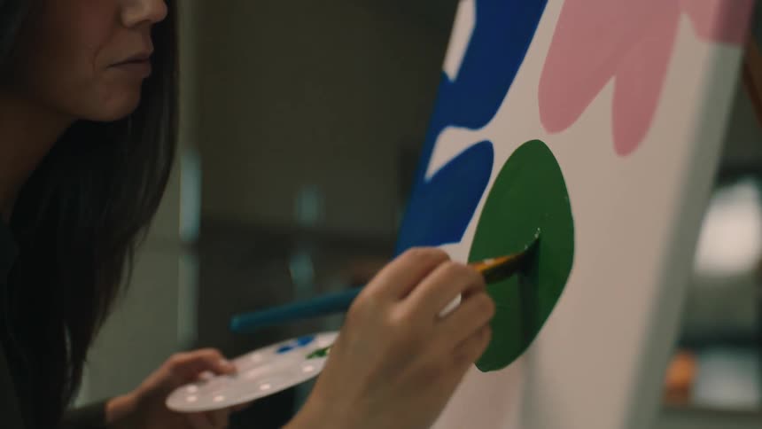 Female artist paints abstract shapes on canvas resting on easel