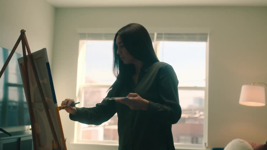 A woman paints on a canvas in her living room