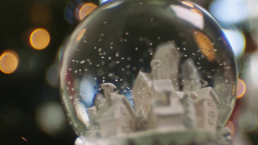 Person holds elaborate snow globe while standing near decorated tree