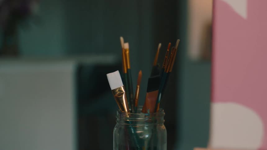 A hand places a paintbrush in a jar