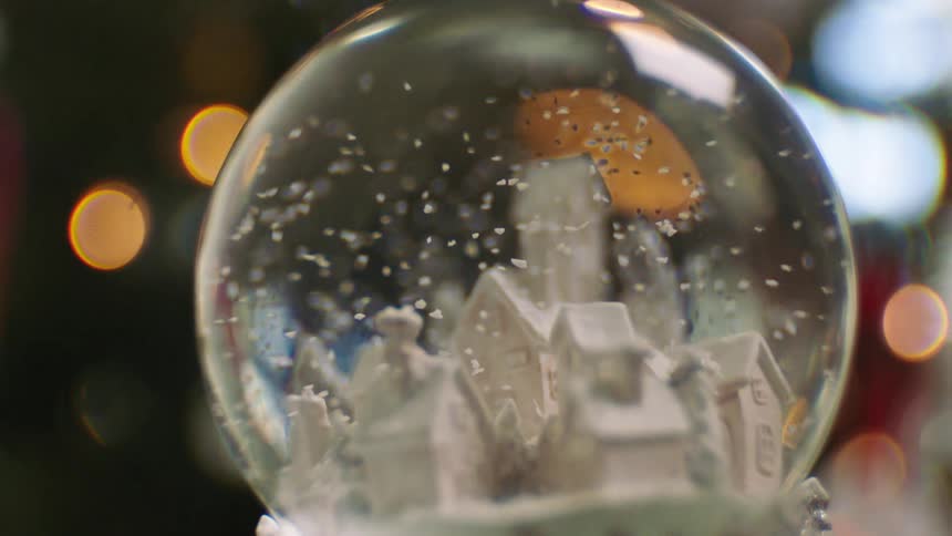 A persons hand holding a toy globe with water and house inside