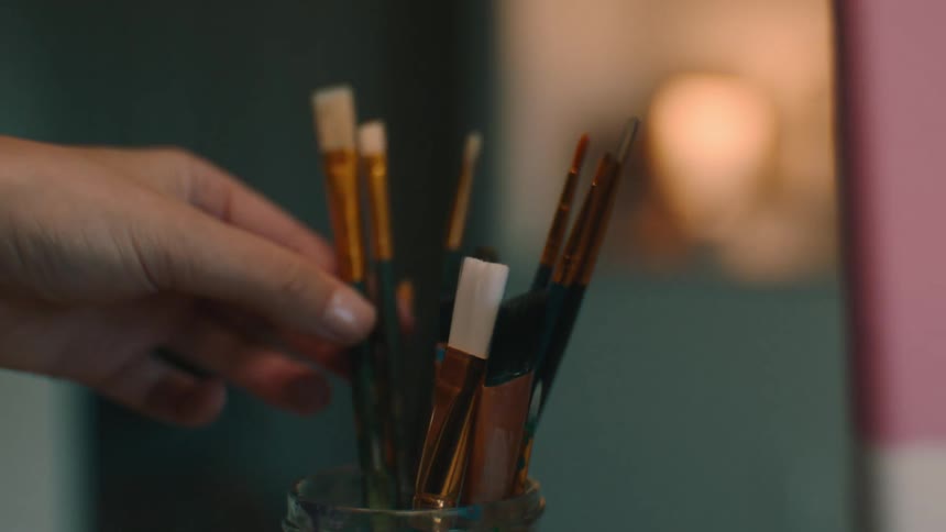 Closeup of a jar with brushes of different sizes and a female hand taking one