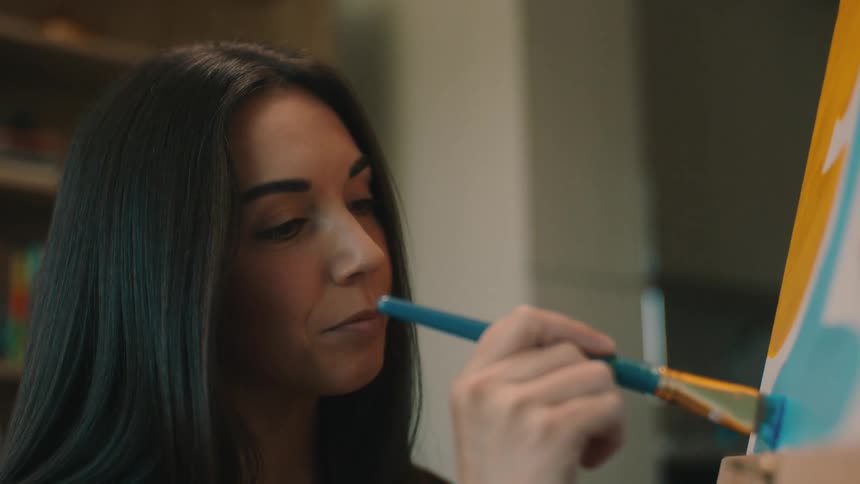 A woman painter is painting a picture using a brush with blue paint