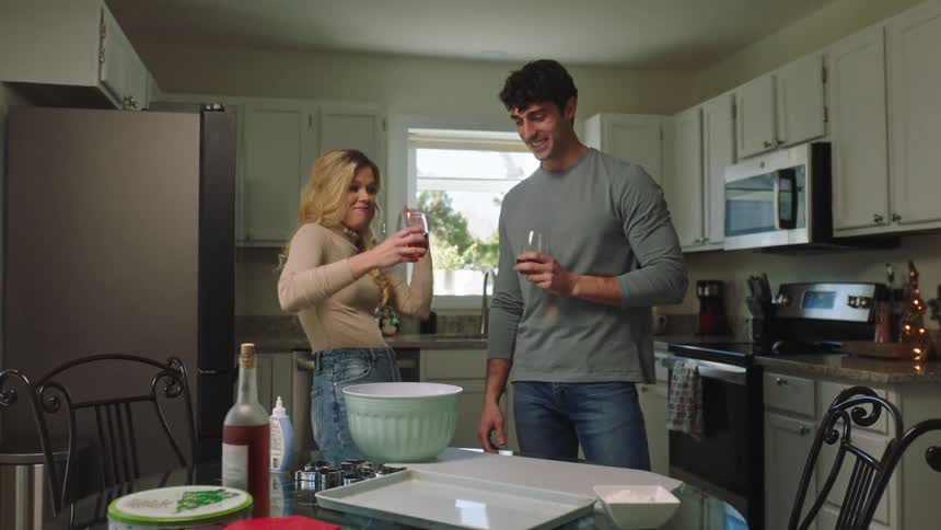 A woman dances a bit for fun with a guy in a kitchen