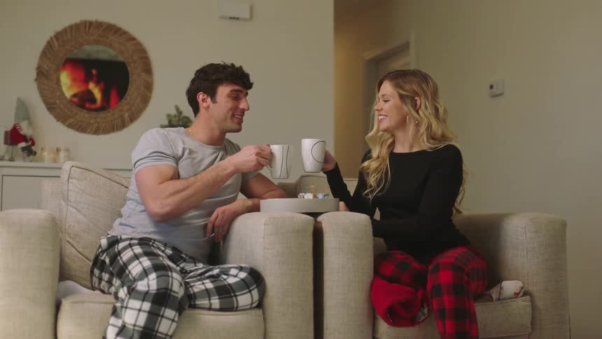 A man and a woman sit in a living room drinking