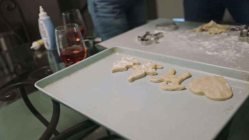 Closeup on a table with cookie dough and molds a bowl with two people around preparing