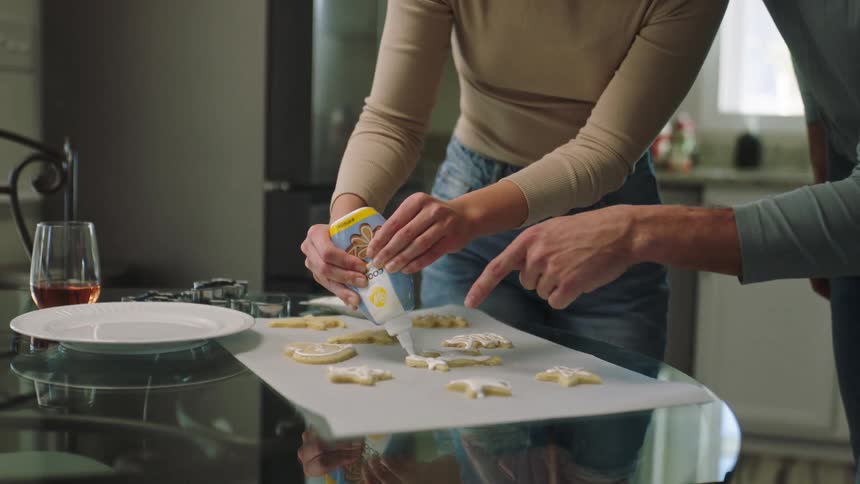 Man watches woman ice cookies using prepared icing at home near kitchen