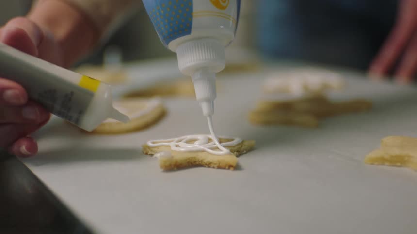Two people apply icing to cookies