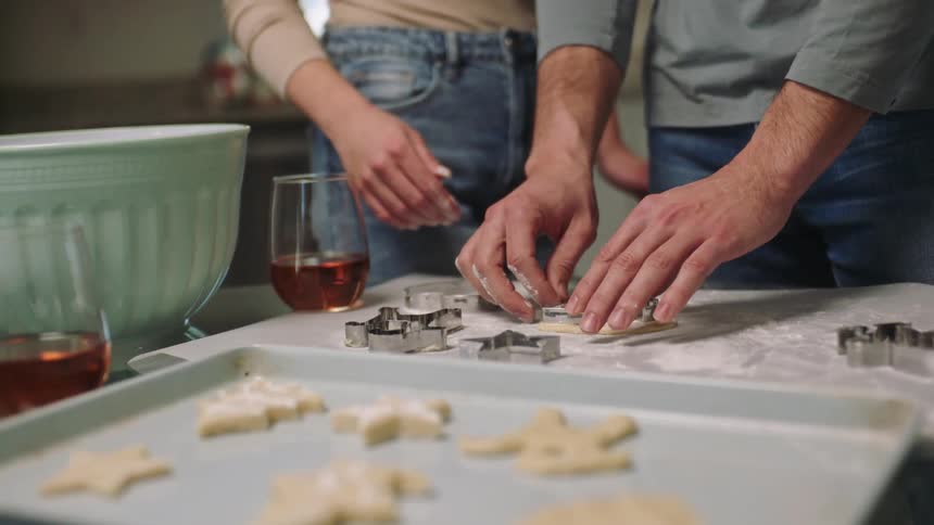 Joyful couple cutting christmasshaped cookie dough
