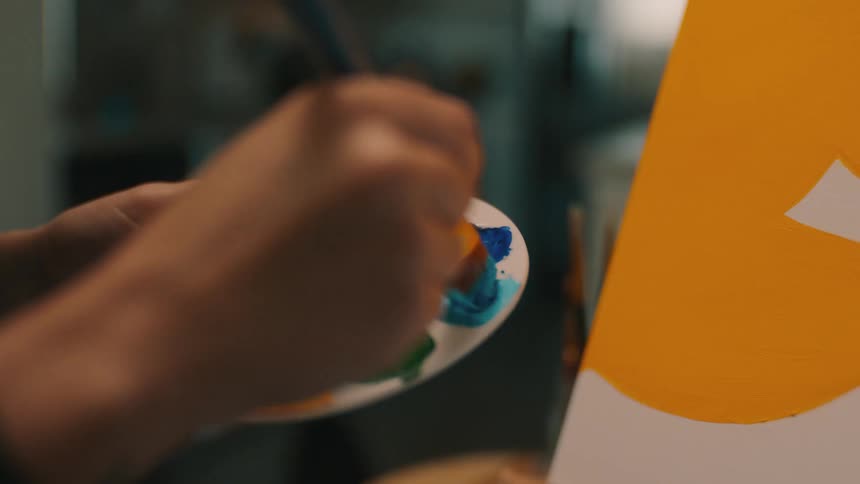 Closeup of a womans hands painting a picture and holding a palette of paints