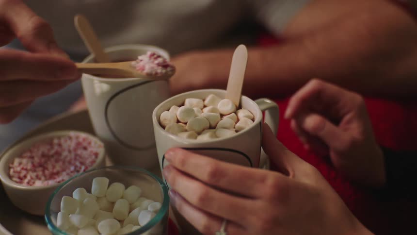 Two people preparing drinks in mugs with marshmallows and candy