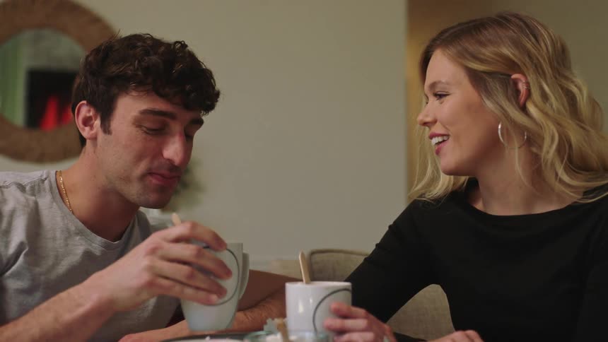 A man and a woman sitting on a couch drinking hot chocolate with marshmallows while talking and laughing