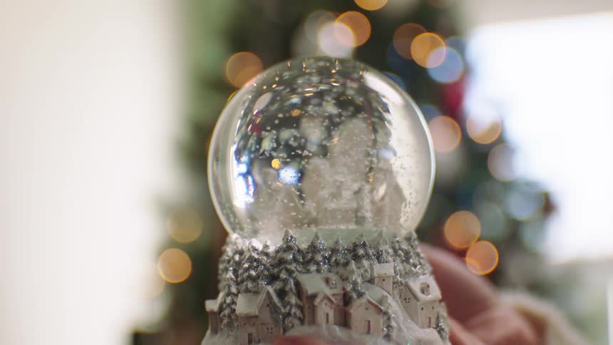 A woman plays with a snow globe in front of a christmas tree