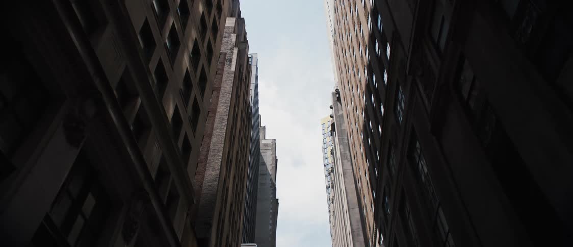 Moving slowly through tall buildings looking up at sliver of sky