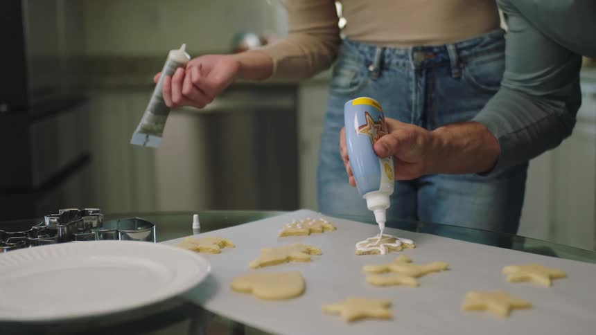 A man and a woman put icing on cookies in a kitchen