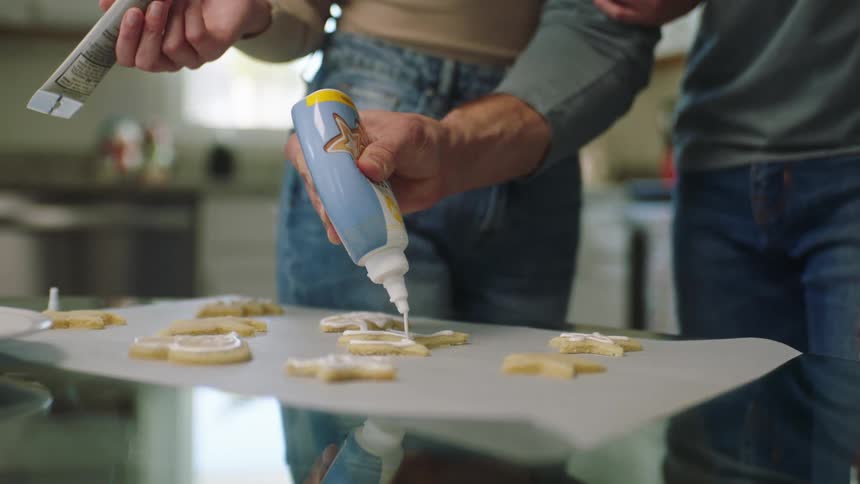Two people are putting frosting on cookies