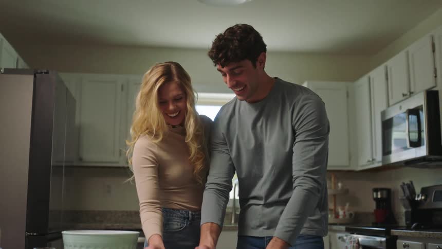 Couple works with cookie dough while standing in kitchen