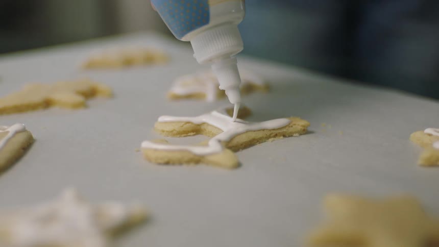 Closeup on a tube pouring icing on top of christmas cookies