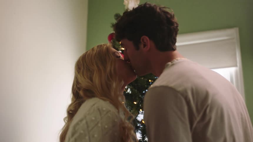 A woman kisses a man in front of a christmas tree