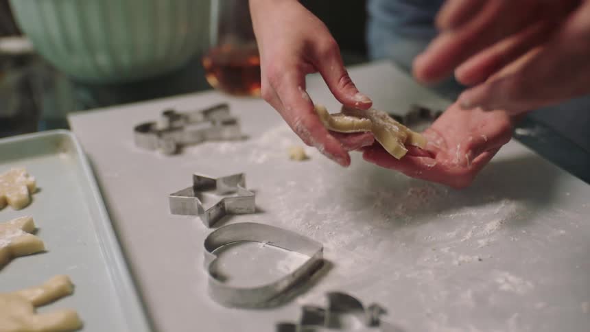 Two people are cutting out sugar cookies and placing them on a baking sheet