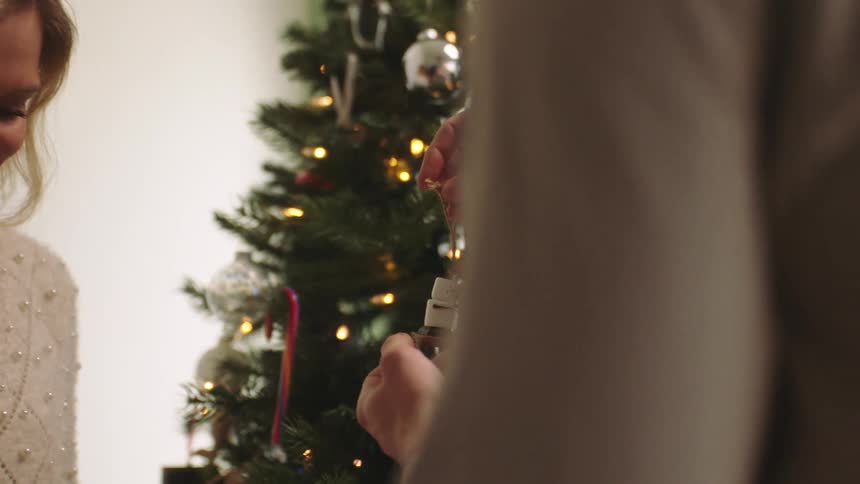 A man takes an ornament from a woman and hangs it on a christmas tree