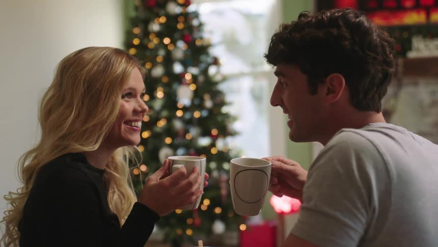 Couple sitting on the living room sofa kissing and drinking a cup of coffee