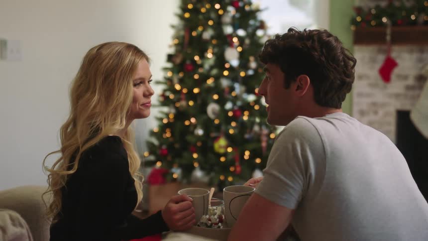 A young couple sit in a living room and drink out of mugs
