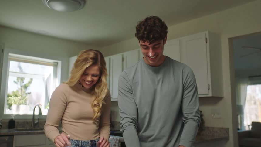 A man and a woman care cooking together when she dabs flower on his nose and laughs hard