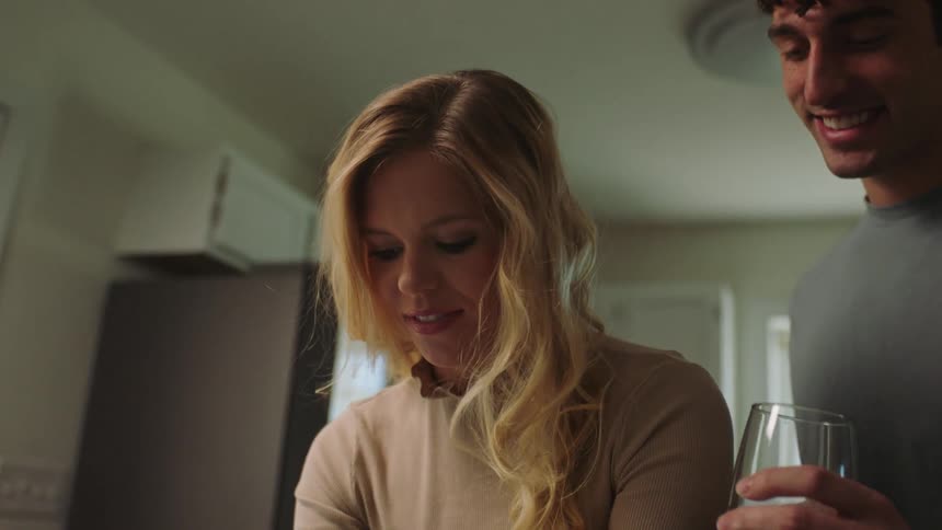 A woman makes cookies as her boyfriend watches with a beverage
