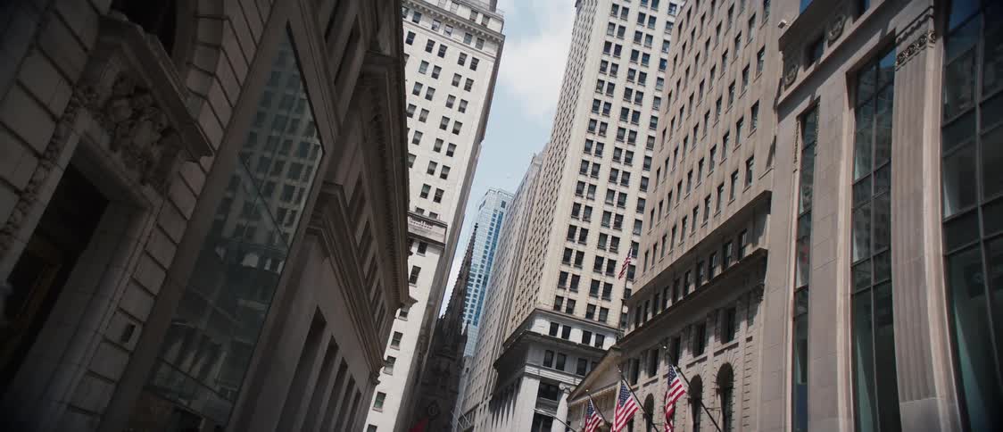 A region of a city with very tall buildings in beige colors and there is a person walking on the sidewalk